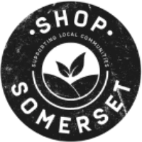 A black circular logo with the text “Shop Somerset” and “Supporting Local Communities”, featuring a plant sprout in the centre above stylised hills.