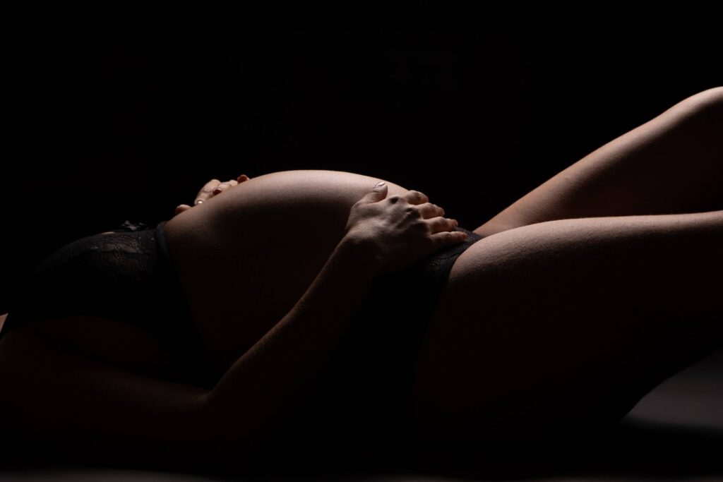 A pregnant woman laying on her back in a dark room.