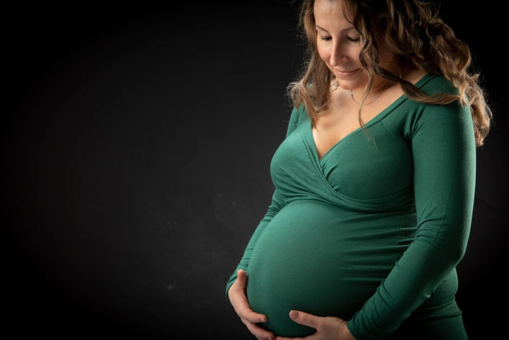 A pregnant woman in a green dress posing against a black background.