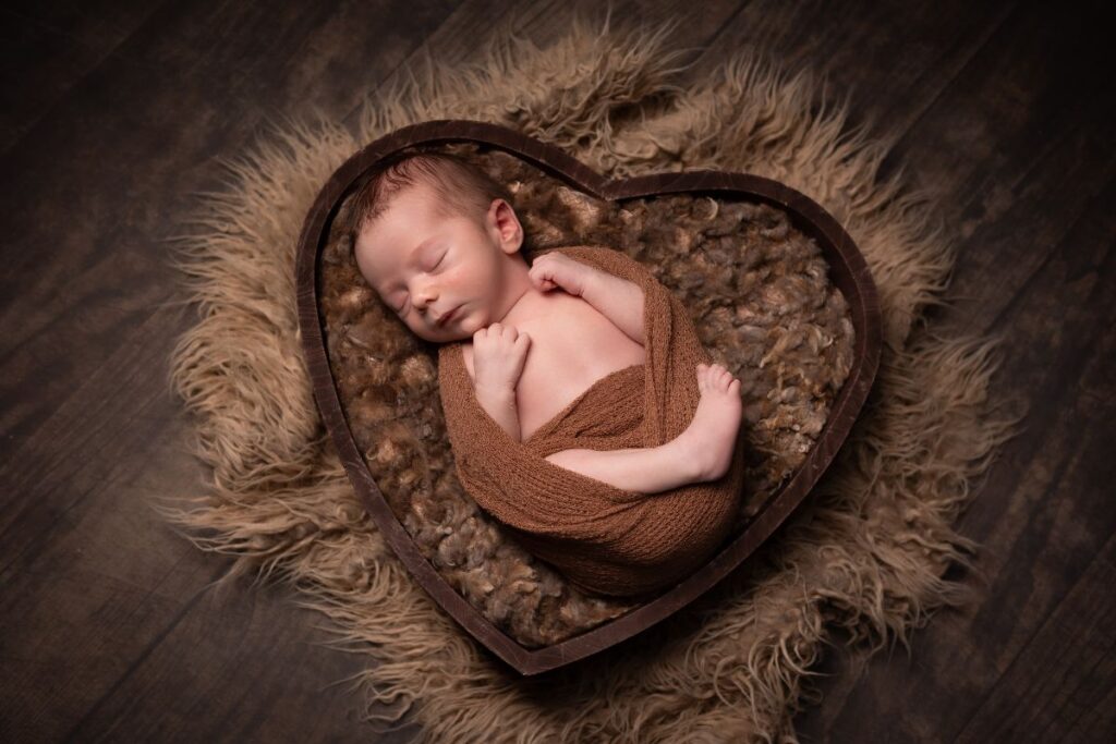 A newborn baby sleeping in a heart shaped box.