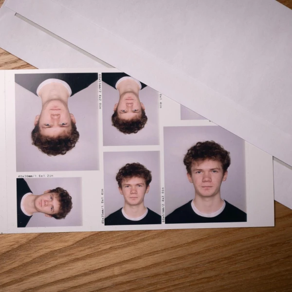 A sheet of six passport-style photos of a young man with curly hair, partially covered by a white envelope, lying on a wooden surface.